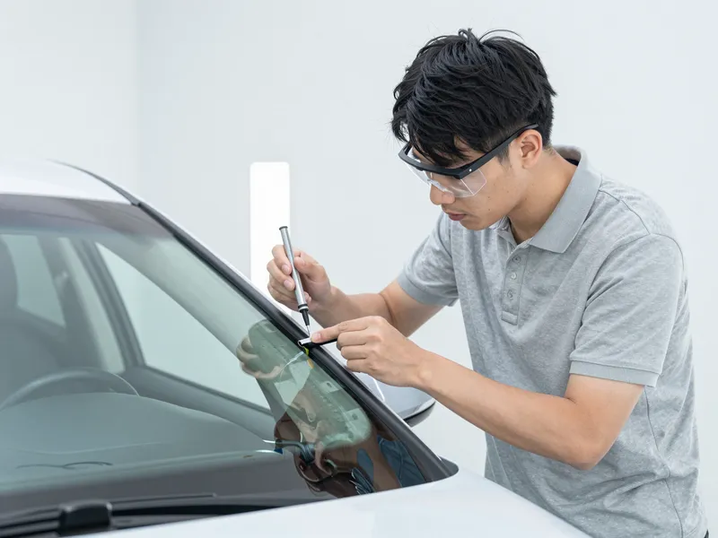 Ein Techniker repariert konzentriert einen kleinen Riss in einer Autoscheibe in einer hellen Werkstatt.