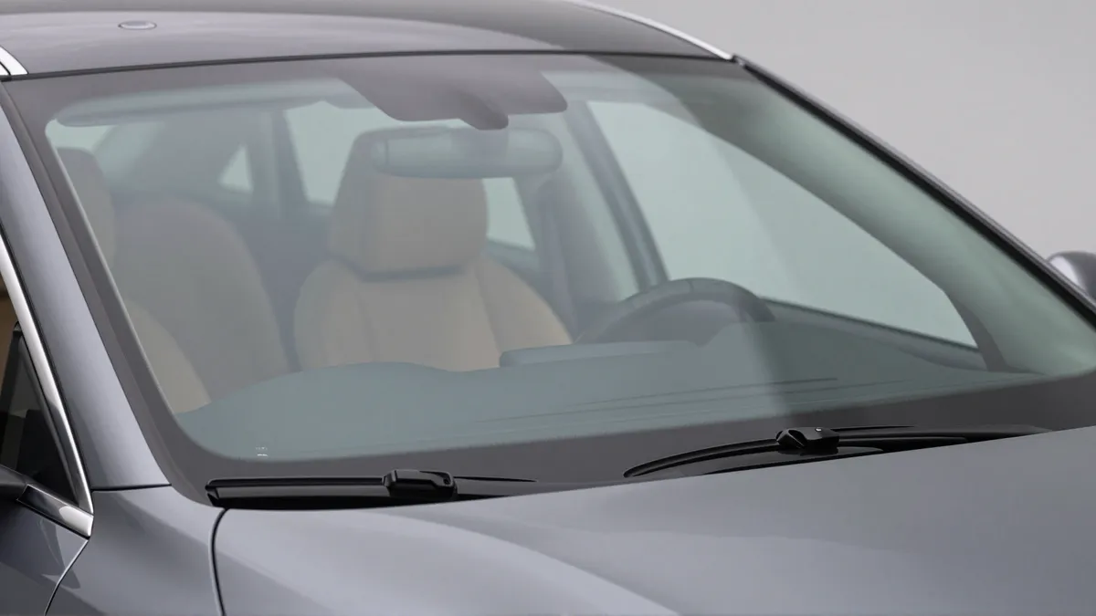 Ein makellos sauberes Autofrontglas spiegelt weiches Licht wider, dahinter ein Lederlenkrad.