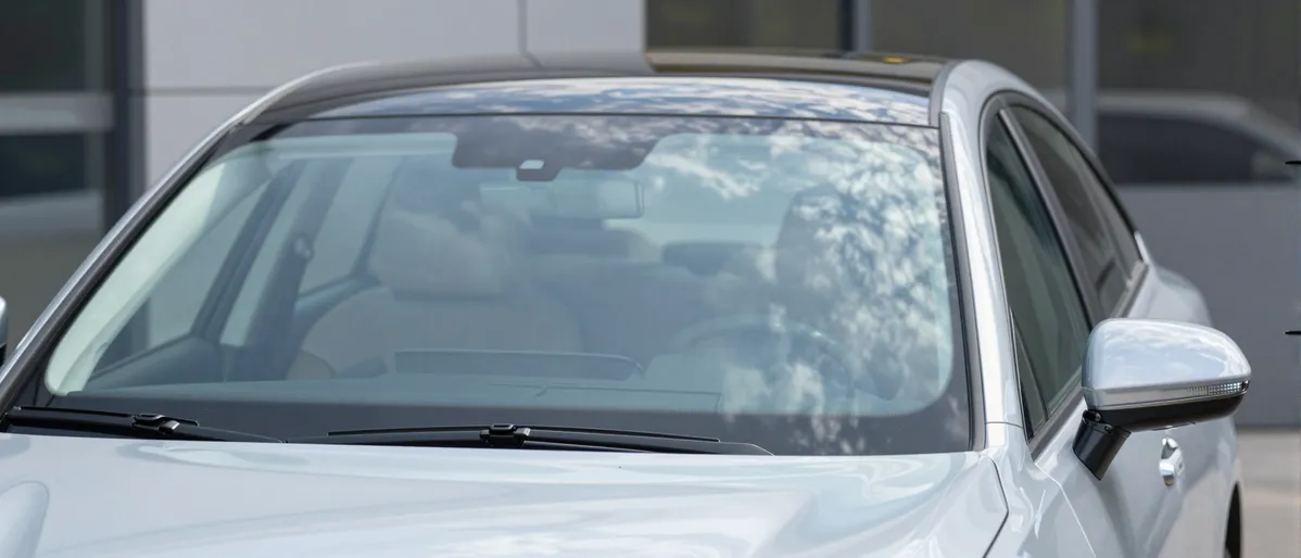 Ein modernes Auto mit makelloser Windschutzscheibe parkt vor einem Autoservicezentrum an einem sonnigen Tag.