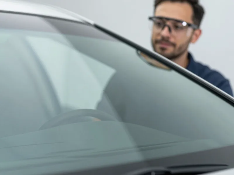 Ein Autoglastechniker prüft mit Schutzbrille die makellose Oberfläche einer neuen Windschutzscheibe in einer Werkstatt.