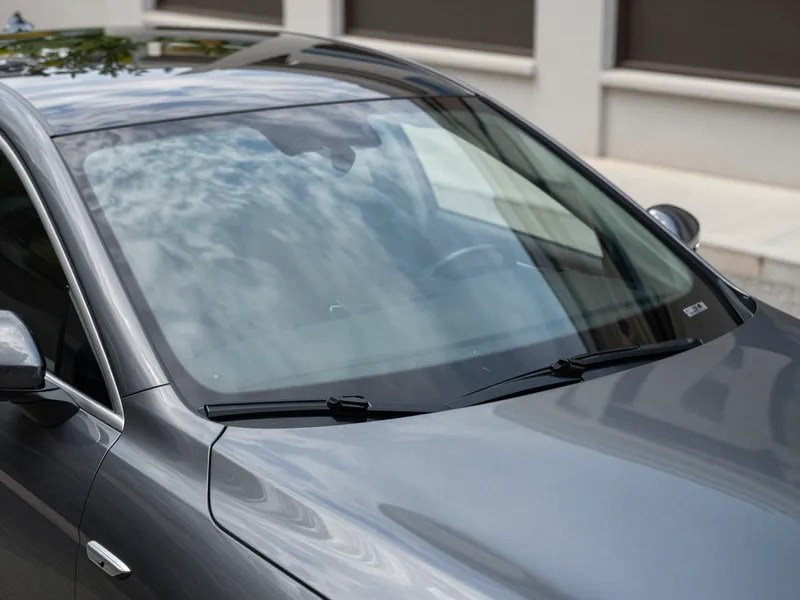 Ein dunkler Luxuswagen mit makelloser neuer Windschutzscheibe steht in einer städtischen Auffahrt.